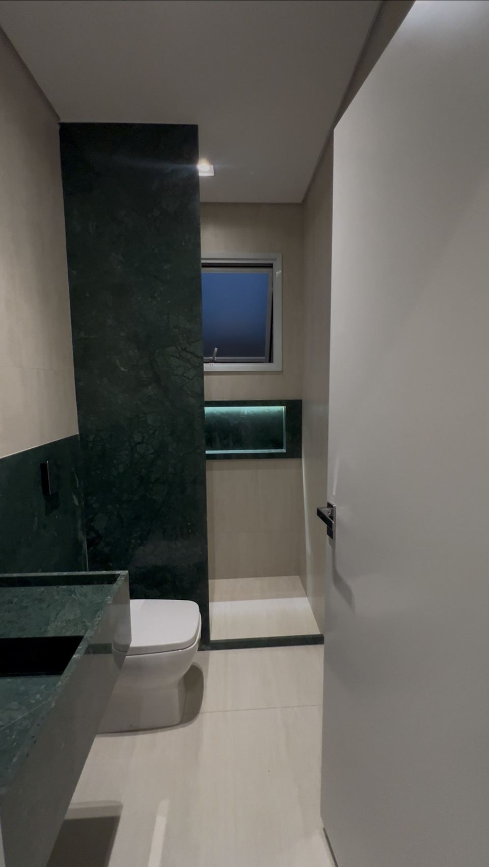 Banheiro com revestimento em pedra verde e nicho iluminado